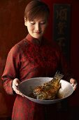 Frau serviert Karpfen aus dem Wok (China)