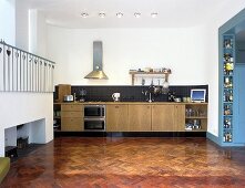 Herring-bone parquet in an open-plan kitchen with a counter unit and a gallery with white balustrade
