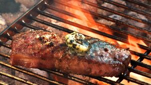 Rump steak with herb butter and onions on a barbecue