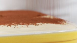 Preparing tiramisu: dusting with cocoa powder