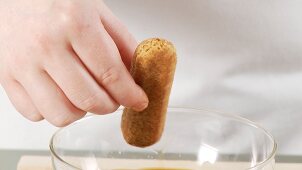 Preparing tiramisu: dunking a sponge finger into espresso and placing in a dish