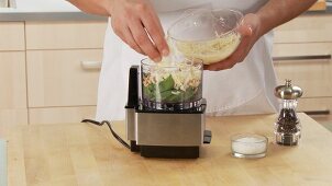 Grated cheese being added to pesto ingredients in a mixer