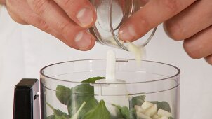 Garlic being added to pesto ingredients in a mixer