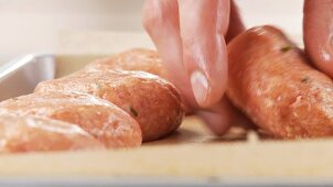 Raw burgers being placed on a baking tray laid with grease-proof paper