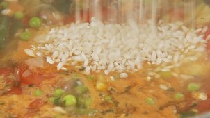 Risotto rice being added to minestrone and being seasoned with pepper