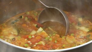 Minestrone being scooped out of a pot with a ladle
