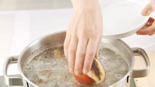 Roasted onion halves being added to a pot of soup