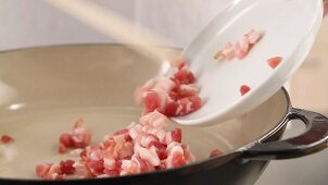 Diced bacon being put in a pan and fried