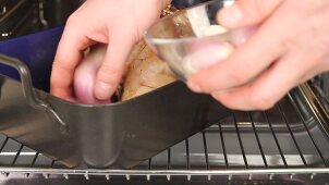 Vegetables and herbs being added to a leg of lamb