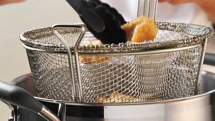 Fried fish fillets being removed from a frying basket