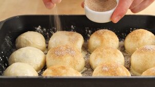 Raw Buchteln (baked, sweet yeast dumplings) being dusted with cinnamon sugar