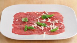 Beef carpaccio being sprinkled with grated parmesan
