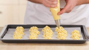 Choux pastry being piped onto a baking tray lined with greaseproof paper