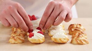 Profiteroles being filled with cream and raspberries