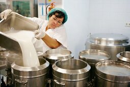 A woman pouring milk into a container in a commercial kitchen