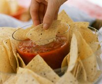 Hand taucht Tortilla-Chip in Salsa-Sauce