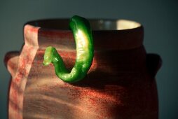 A Long Green Hot Pepper Hanging Off a Pot
