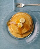 Pancakes mit Bananen und Ahornsirup auf Glasteller