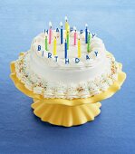 A Birthday Cake on an Yellow Stand with Lit Candles