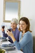 Two Women Holding Glasses of Red Wine While Sitting at Hanukkah Diner Table