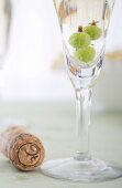 Glas Prosecco mit Stachelbeeren, daneben Korken