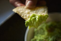 Hand hält Tortillachip mit Guacamole