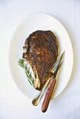 Rib Eye Steak on a White Plate; Rosemary Sprig; Knife and Fork