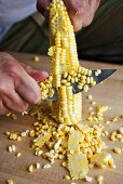 Mann schneidet Maiskörner vom Maiskolben