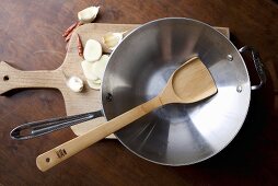 An Empty Wok and Wooden Spoon; On Cutting Board; Garlic