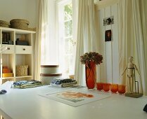 Arbeitstisch mit gestapelten, runden Schachteln, Tischwäsche, einer Blumenvase mit getrockneten Hortensien und einem Holzmodell