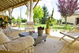 Weitläufige, überdachte Gartenterrasse mit gemütlichen Möbeln und mit Blick auf den sonnigen Garten