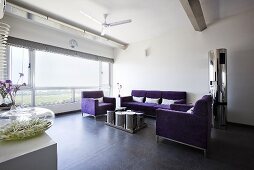 Sitzecke mit lila Couchgarnitur & Tisch aus Edelstahl vor breiter Fensterfront