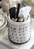 Cutlery in a porcelain pot in a metal basket