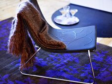 Wollschall auf Stuhl mit blauer Sitzschale und Metallgestell auf schwarz blauem Teppich mit Blumenmuster