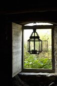 Lantern in a open window hanging on a lintel with wooden shutters on the inside and a view onto a garden