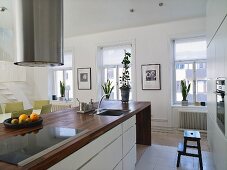 White designer kitchen - stainless steel vent over a countertop with a wooden working area and window wall