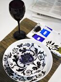Glass bowl decorated with a black and white design and black stemware on a placemat