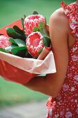 Frau hält in Papier gewickelten Blumenstrauss mit Protea