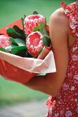 A woman holding a bunch of protea flowers wrapped in paper