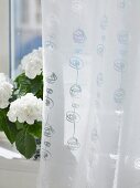 Weisser Vorhang und Blumentopf auf Fensterbank