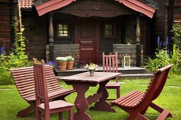 Red garden furniture on a field with an old weekend house with a veranda in the background