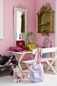 A corner of a child's room - a white bench and table in front of a mirror hanging on a pink wall