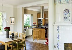 A dining area and an old tiled stove in front of an open-plan kitchen with a view of a counter