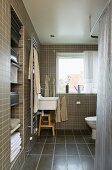 Brown mosaic tile in a bathroom and built in niche with hand towels and view of the sink at the window