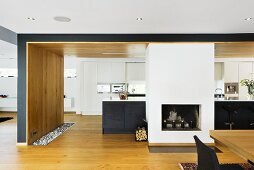 Open plan kitchen with fireplace in front of a black kitchen unit and white built in cupboard