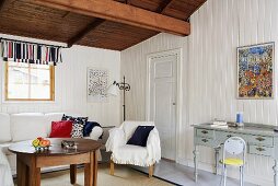 A living room in a country house with white wood panelling and a wooden ceiling