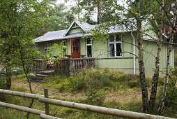 A green wooden house in a forest with a red front door and a stone terrace