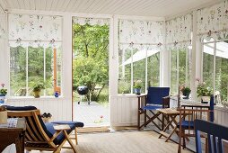 Wooden chairs in a conservatory with white wooden panelling and floral fabric blinds at the windows