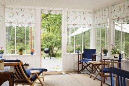 Holzstühle im Wintergarten mit weisser Holzverkleidung und geblümten Stoffblenden am Fenster