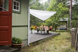 A wooden house with a terrace and a sunshade over garden furniture